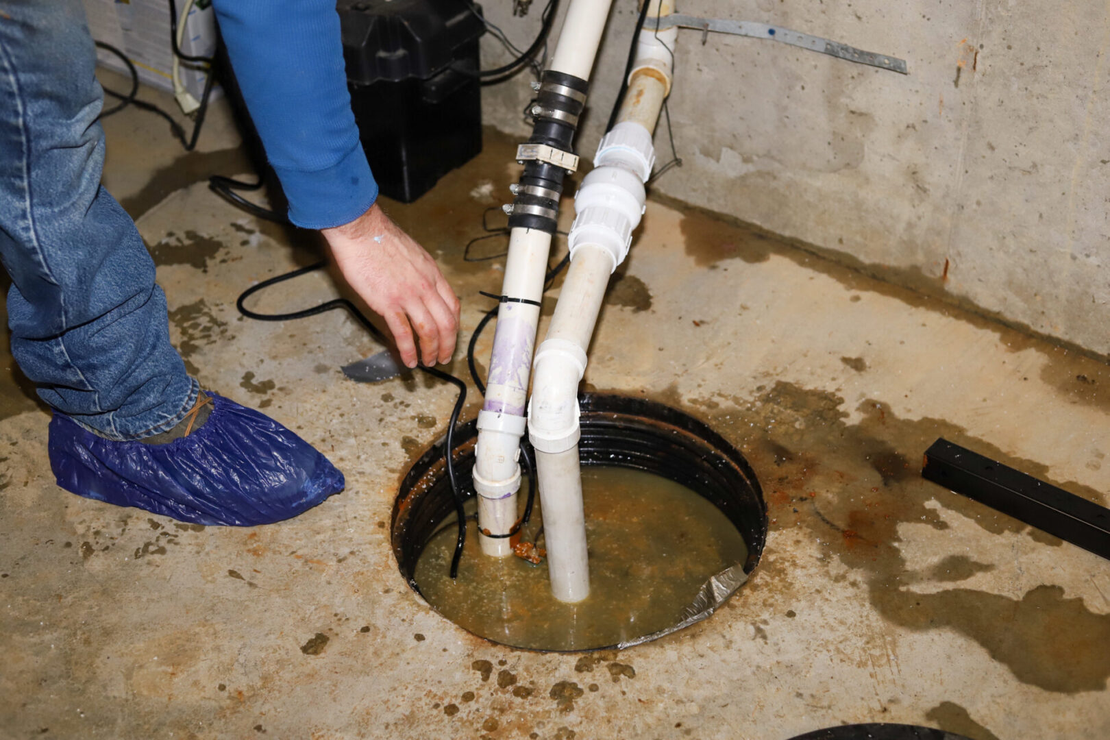 A plumber repairing a sump pump in a flooded basement in a resi